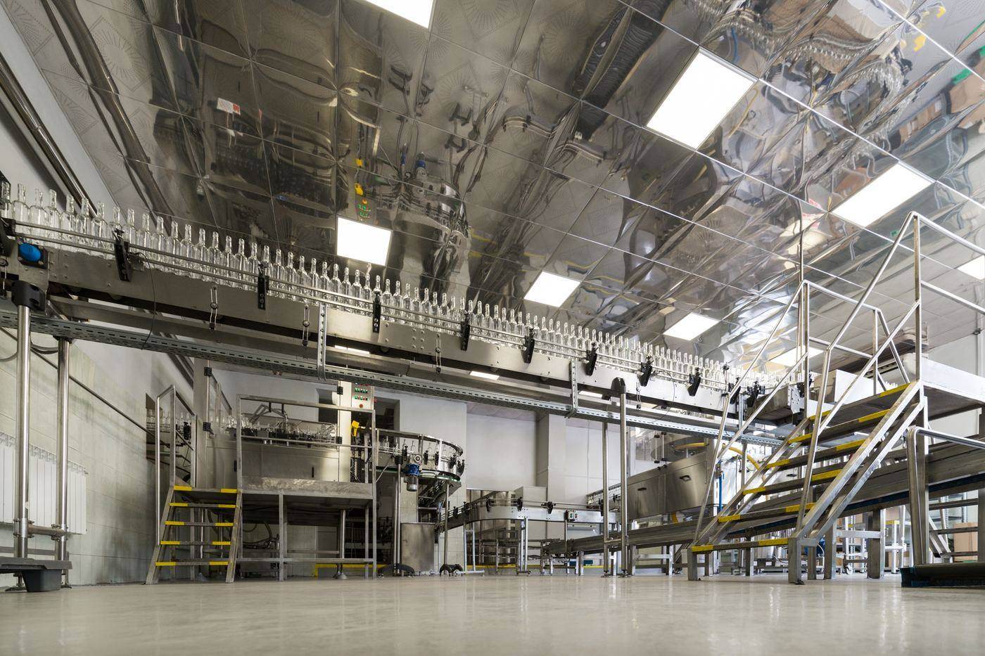 A stainless steel packing hall, with an overhead conveyor carrying containers above the filling line