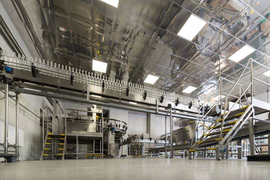 A stainless steel packing hall, with an overhead conveyor carrying containers above the filling line