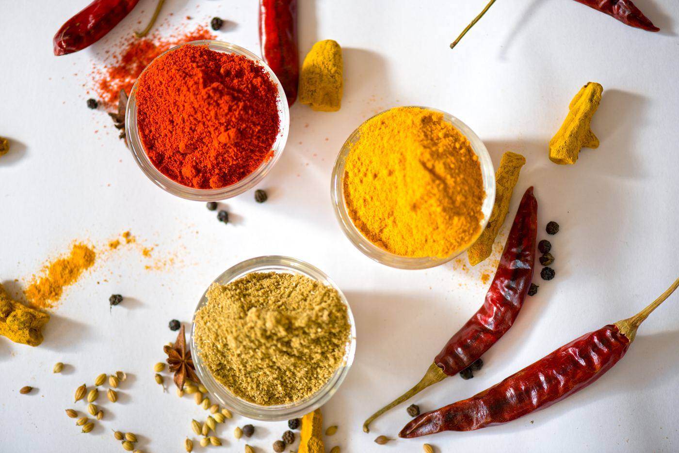 Bowls of red chilli, turmeric and coriander powder beside whole dried chillies, peppercorns, coriander seed and turmeric fingers
