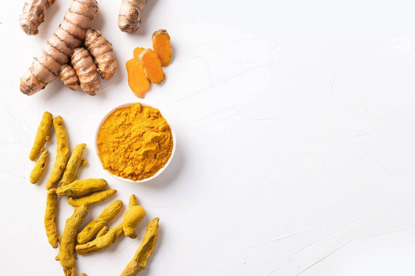 Turmeric fingers, fresh rhizome and a bowl of milled turmeric powder laid out on a pale table